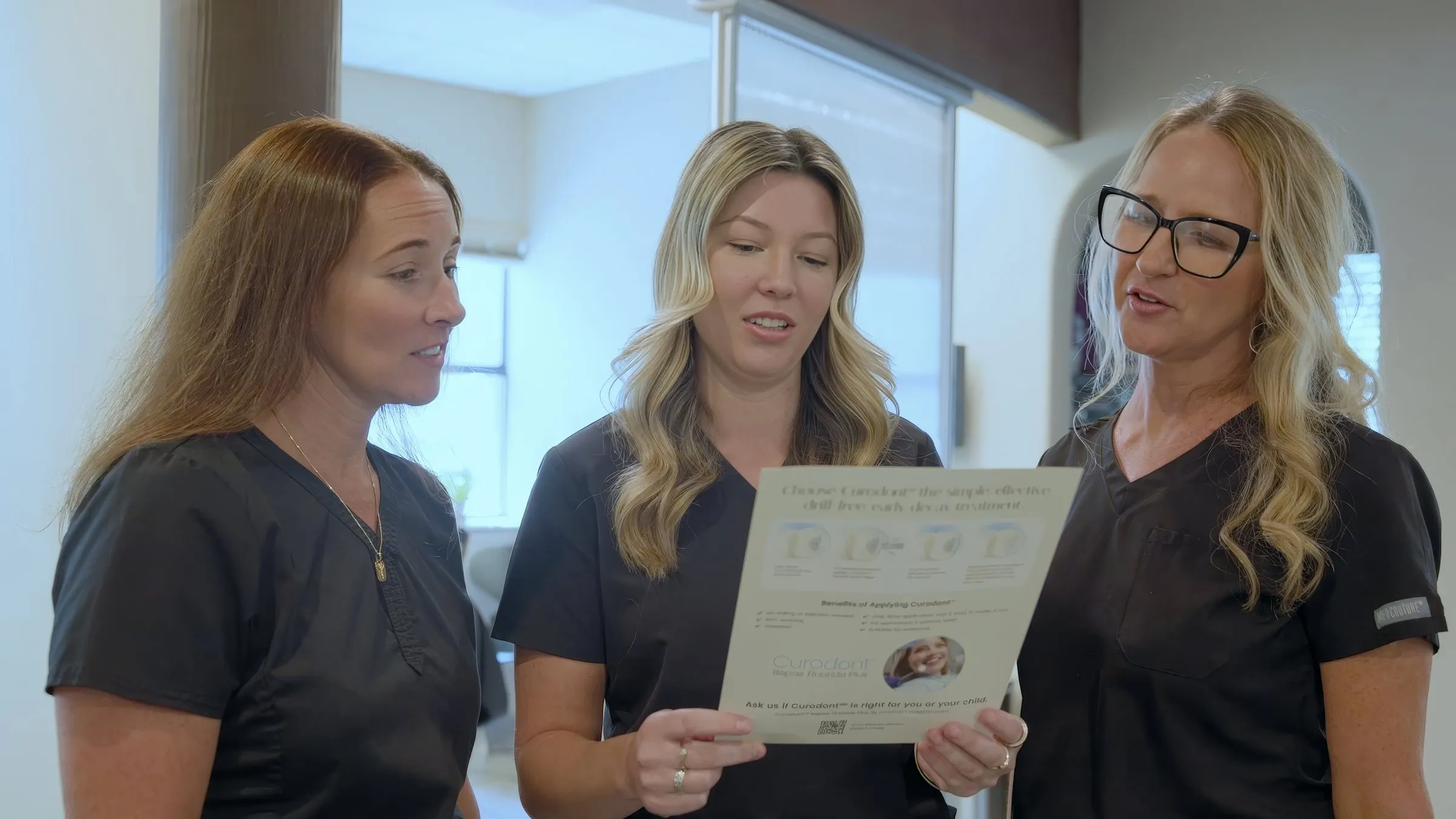 Three Cardinal Point Dental team members reading a handout together — fluoride treatment in Jacksonville, FL