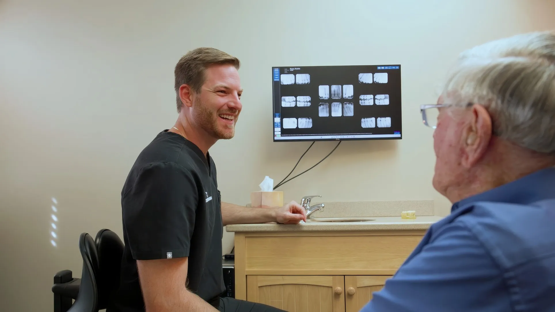 Dr. Dillon Hernandez smiling as he talks with a patient beside a monitor of exam X-rays at Cardinal Point Dental, Jacksonville, FL (teeth cleanings and exams)